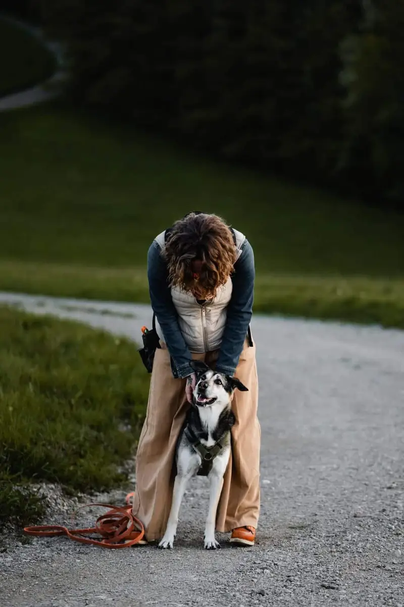 Almut beugt sich auf einem Feldweg liebevoll über ihren Hund