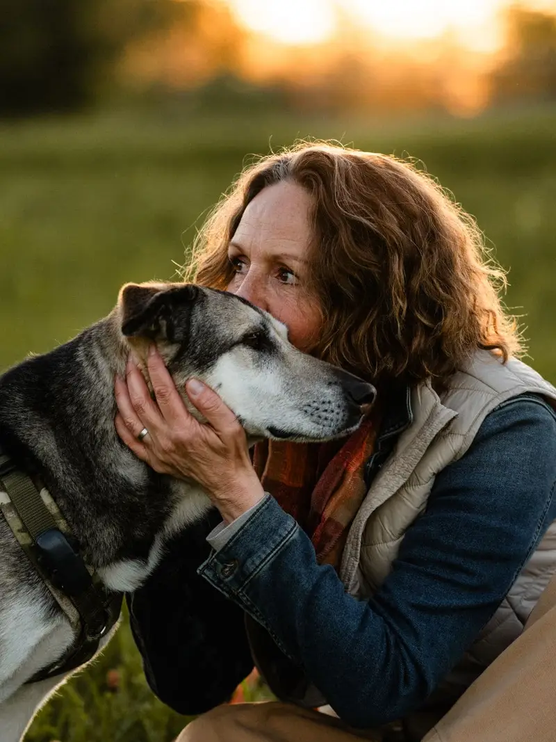 Almut hält liebevoll den Kopf ihres Hundes Ylva im Gegenlicht