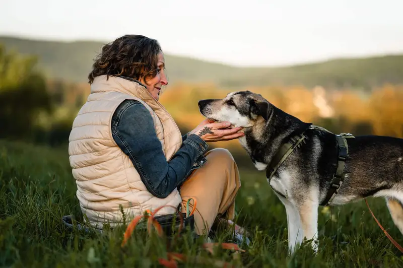 Almut sitzt im Gras, ein Tierschutzhund kommt ihr vertrauensvoll entgegen