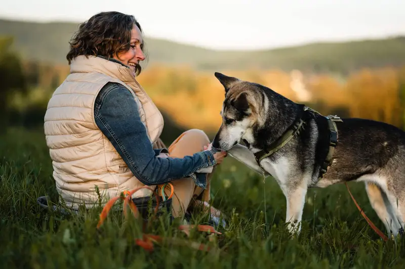 Almut sitzt im Gras, ihr Hund schnuppert vertrauensvoll an ihrer Hand