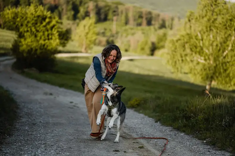 Almut geht in die Hocke und lobt ihren Hund an der Leine auf einem Feldweg