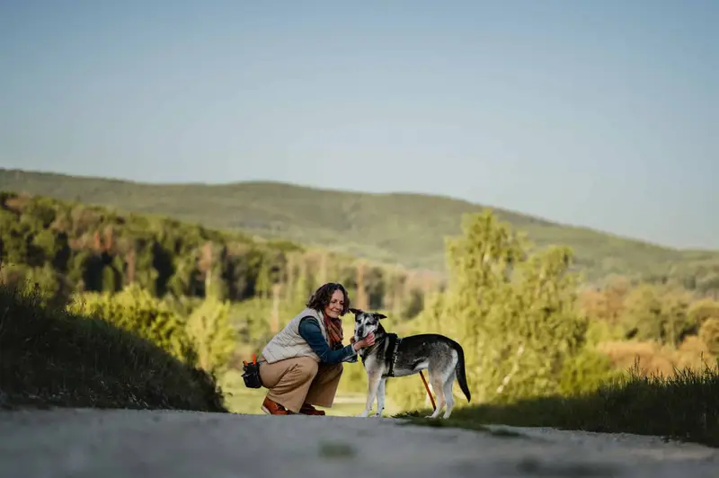 Almut hockt auf einem Weg in den Hügeln und belohnt ihren Hund